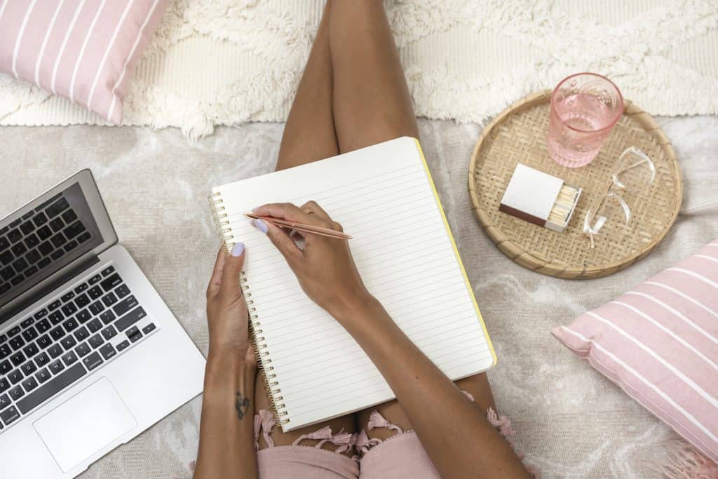 Woman sitting and writing with notebook and laptop