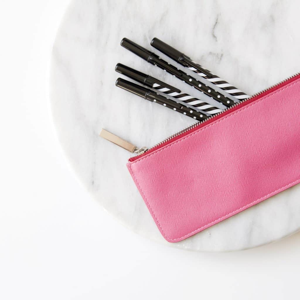 Flatlay image of pink leather pouch with pens on round marble slab