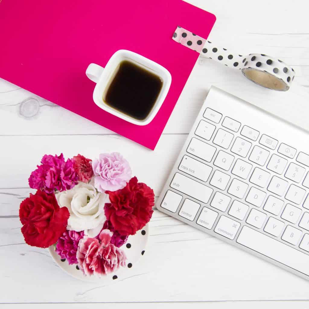 White keyboard and cup of coffee, pink and red flowers