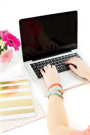 woman's hands typing on laptop with floers and journal nearby