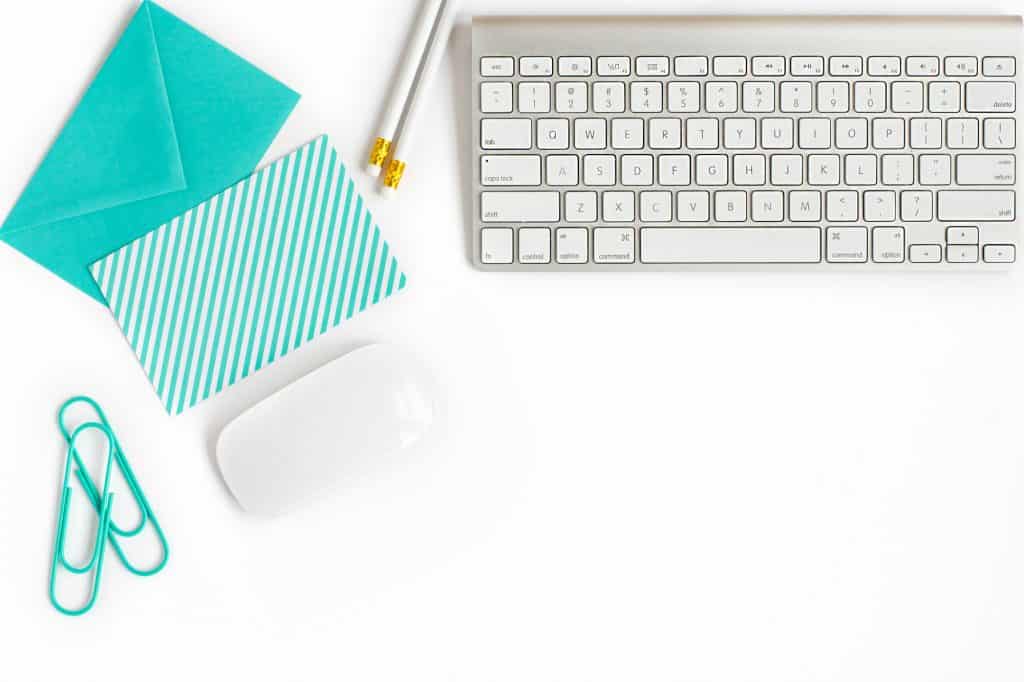 Flatlay with white keyboard, notecard, pencil and paperclips