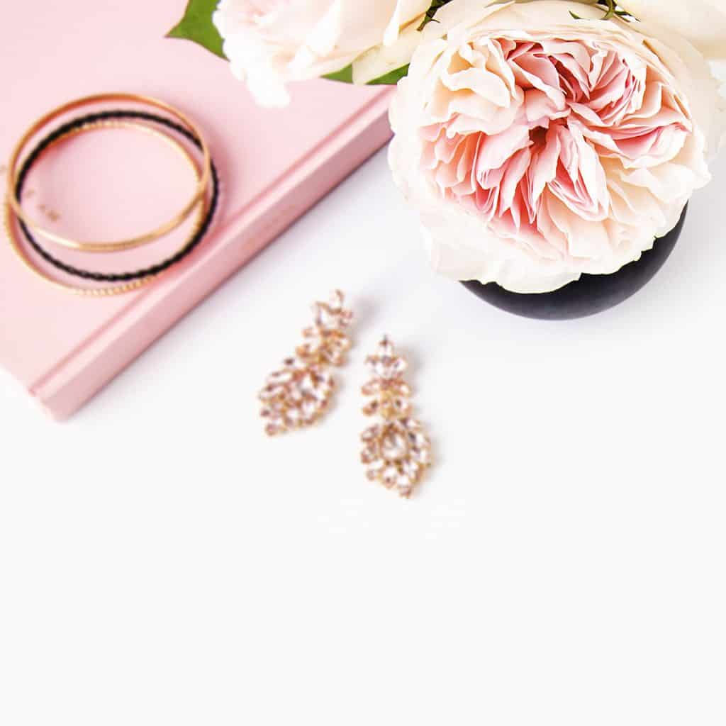 Pink notebook with bracelets on top, fancy earrings, and pink peonies