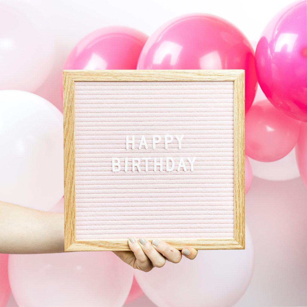 woman holding happy birthday sign with balloons in back