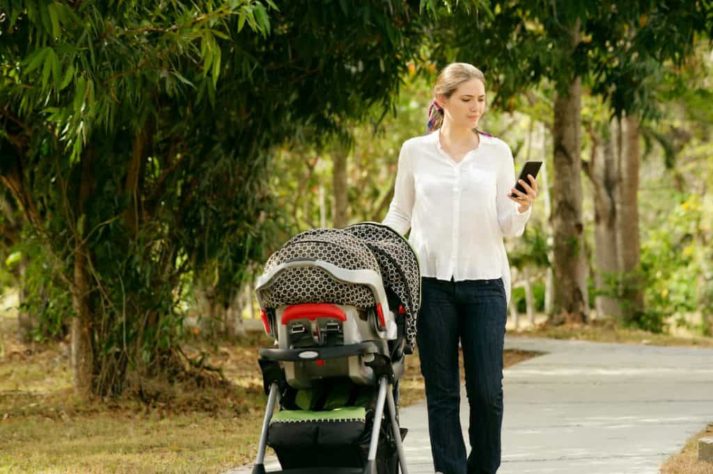 Woman pushing stroller in park and looking at smartphone