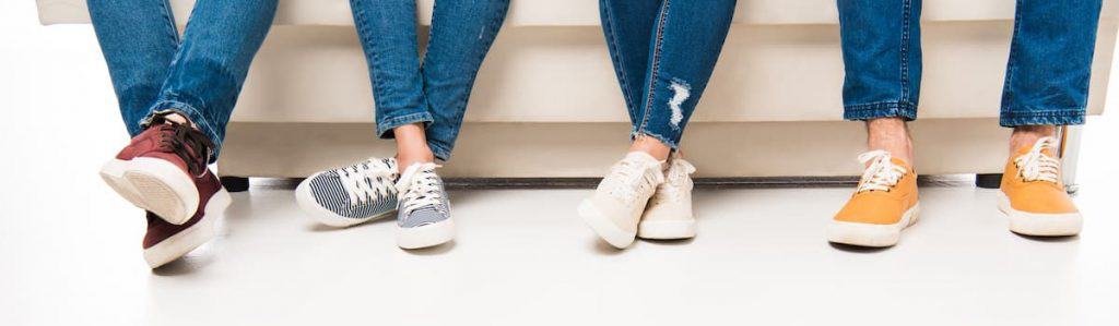 Image of four women's feet in tennis shoes sititng on coach